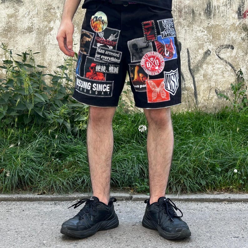 Puede incluir: Pantalones cortos de mezclilla negros con m&uacute;ltiples parches con varios dise&ntilde;os y texto. Los parches incluyen una mariposa, una calavera y el texto "MISSING SINCE". Los pantalones cortos se usan con zapatillas negras.