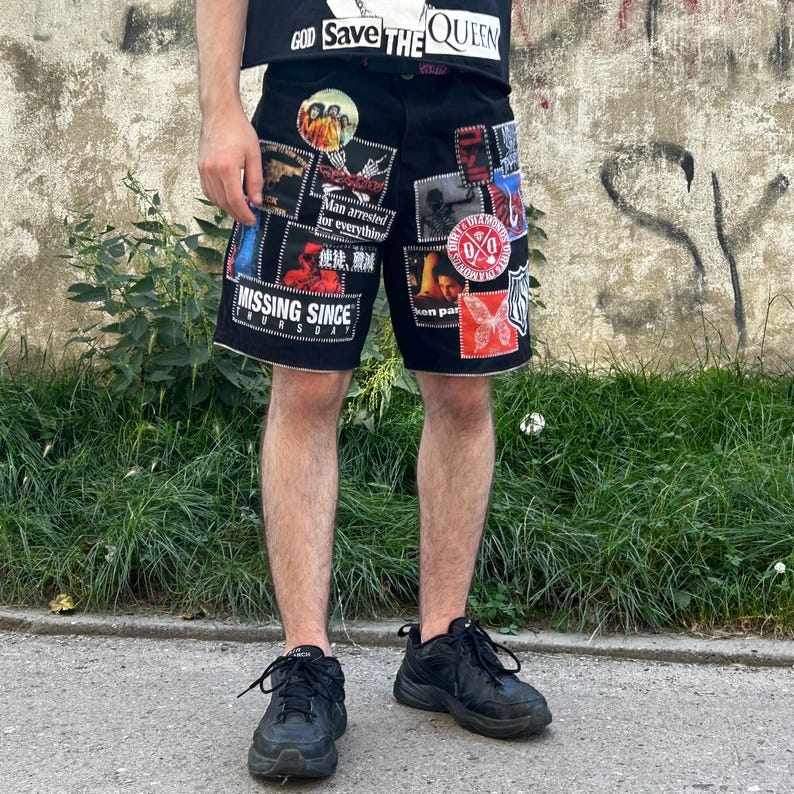 Puede incluir: Pantalones cortos de mezclilla negros con varios parches y texto. Los parches incluyen im&aacute;genes y texto como "Man arrested for everything" y "Missing Since Thursday". Los pantalones cortos se usan con una camiseta negra que dice "GOD SAVE THE QUEEN".
