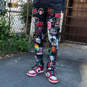 May include: Black denim jeans covered in various patches with red, white, and black designs. The jeans are paired with red, white, and black sneakers. The patches feature images and text in multiple colors.