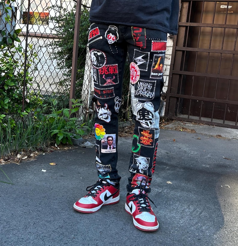 May include: Black denim jeans covered in various patches with red, white, and black designs. The jeans are paired with red, white, and black sneakers. The patches feature images and text in multiple colors.