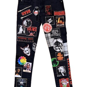 Peut inclure: Jean en denim noir orné de nombreux patchs avec du texte et des graphiques. Les patchs incluent les mots "DEAD", "missing since", "OLDBOY" et "AKIRA". Le jean a une fermeture à bouton et à glissière.