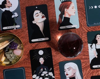 Może przedstawiać: Zestaw kart tarota z ilustracjami kobiet i elementami niebieskimi. Karty są czarne z białym tekstem i obrazami, w tym "Ace of Pentacles", "The Star", "The Empress" i "The Sun". Przezroczysta kryształowa kula i mała miska z kryształami są również obecne.