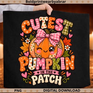 Może przedstawiać: Czarna koszulka z grafiką mrugającej pomarańczowej dyni z różową kokardą w kratkę. Tekst głosi CUTEST PUMPKIN IN THE PATCH. Projekt zawiera kolorowe wzory, motyw panterki oraz jesienne liście jako elementy dekoracyjne wokół grafiki.
