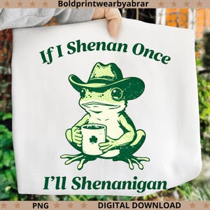 Puede incluir: Camiseta blanca con un diseño de una rana verde con sombrero de vaquero y una taza con un trébol. El texto dice "If I Shenan Once I'll Shenanigan". Es una descarga digital.