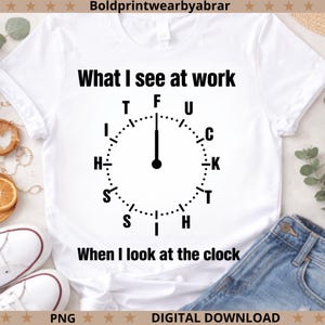 May include: White t-shirt with the text "What I see at work" above a clock design. The clock's hands point to the word "F". Below the clock is the text "When I look at the clock".