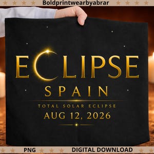 May include: A black fabric item featuring gold text that reads ECLIPSE SPAIN TOTAL SOLAR ECLIPSE AUG 12, 2026. The letter C in ECLIPSE is replaced by a glowing gold crescent moon. Small gold stars are scattered across the black background.