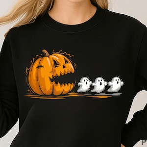 Puede incluir: Sudadera negra con un diseño de Halloween. El gráfico muestra una gran calabaza naranja con una cara tallada y tres pequeños fantasmas blancos. La ilustración tiene un estilo de dibujos animados.