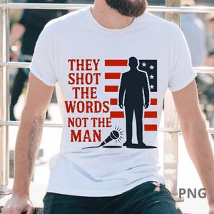 Puede incluir: Camiseta blanca con un diseño gráfico. El texto "THEY SHOT THE WORDS NOT THE MAN" es rojo. El diseño incluye la silueta de una persona frente a una bandera americana estilizada y un micrófono.
