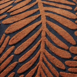May include: Close-up of a rug with a repeating leaf pattern. The leaves are a warm, rust-orange color and are raised above the dark navy blue background. The rug has a soft, textured appearance.