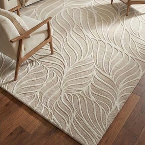 May include: Beige area rug with a leaf pattern. The rug features a raised, textured design in a lighter beige color against a darker beige background. The rug is rectangular and sits on a dark wood floor.