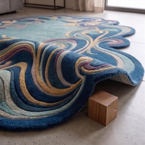 May include: An irregularly shaped area rug featuring a tufted, multi-layered design with swirling patterns in shades of deep blue, light blue, cream, and soft purple. The rug is folded over at one edge, revealing its thick texture and construction.