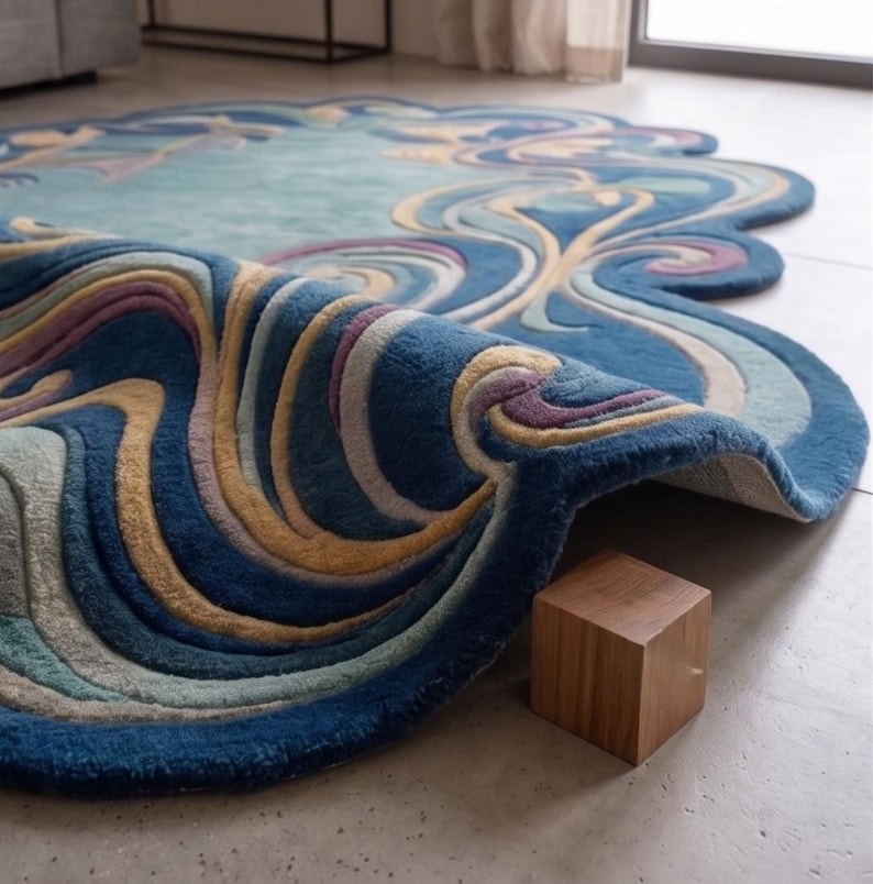 May include: An irregularly shaped area rug featuring a tufted, multi-layered design with swirling patterns in shades of deep blue, light blue, cream, and soft purple. The rug is folded over at one edge, revealing its thick texture and construction.
