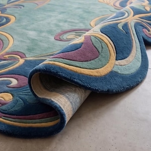May include: A plush area rug with a curved, scalloped edge, featuring a vibrant pattern of swirling organic shapes in shades of deep blue, teal, soft purple, and golden yellow. The rug is partially folded, revealing a woven beige backing.