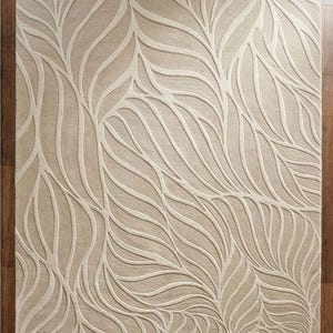 May include: Beige area rug with a leaf pattern. The rug features a repeating design of stylized leaves in a lighter beige color against a darker beige background. The rug is rectangular and appears to be made of a soft material.