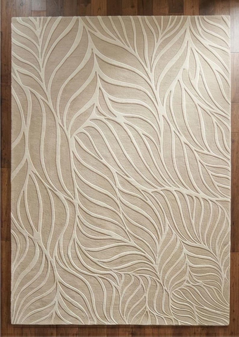 May include: Beige area rug with a leaf pattern. The rug features a repeating design of stylized leaves in a lighter beige color against a darker beige background. The rug is rectangular and appears to be made of a soft material.