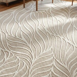 May include: Beige area rug with a raised leaf pattern. The rug features a neutral color palette with a light beige background and off-white leaf-like designs. The rug is placed in a living room setting.