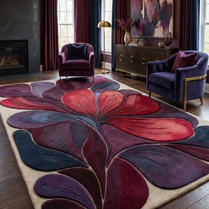 May include: A large, floral-patterned area rug in shades of red, purple, and blue dominates the room. The rug's design resembles a stylized flower, with a cream-colored border. Two purple armchairs and a dark wood cabinet complete the room's decor.