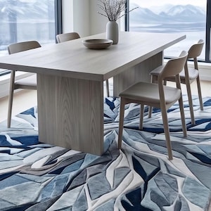 May include: A modern dining room set featuring a light wood rectangular table with four matching chairs. A decorative rug with a blue and white geometric pattern is beneath the table and chairs. A vase with branches and a bowl are on the table.