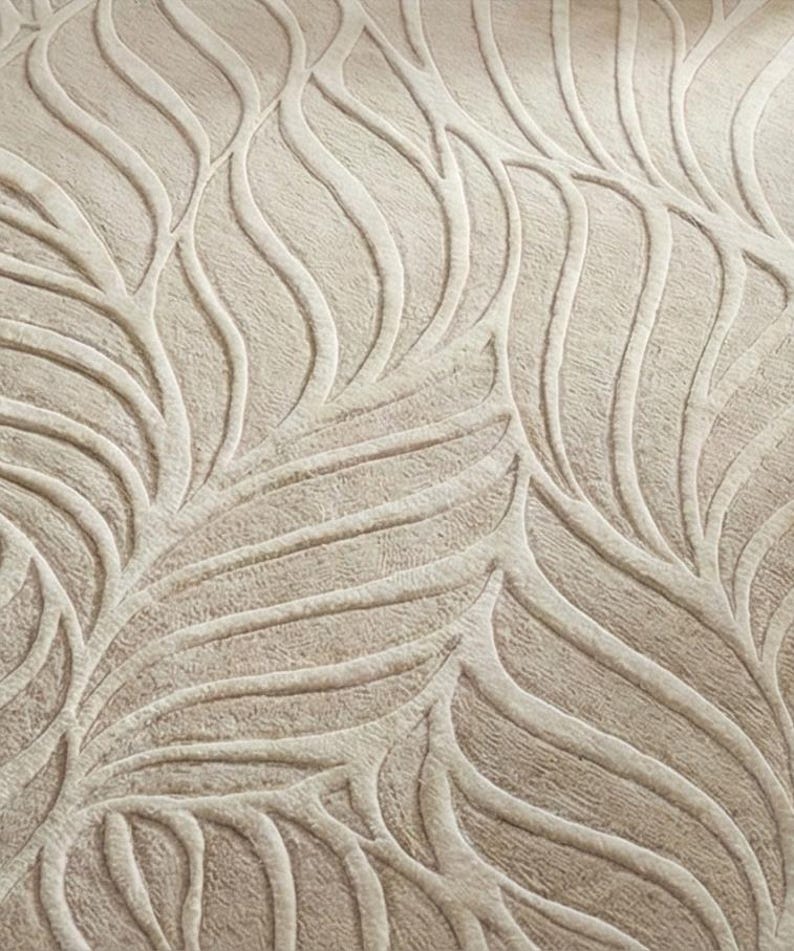 May include: Close-up of a beige textile with a raised, leaf-like pattern. The design features flowing, curved lines and textured details, creating a natural, organic aesthetic. The neutral color palette makes it versatile for various home decor applications.
