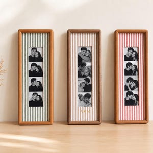 May include: Three rectangular wooden photo frames standing upright. Each frame contains a vertical strip of four black and white photos of a couple. The frames feature fabric backings with green, beige, and red vertical stripes. The center frame has A & M.