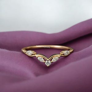 May include: A gold-colored ring with a V-shaped design, featuring multiple clear gemstones. The ring is set against a purple fabric background. The text "NahidSilverjewelry" is visible on the ring.