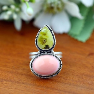 Peut inclure: Une bague en argent avec deux pierres superposées serties dans des bordures en métal torsadé. La pierre supérieure est une gemme vert clair en forme de poire, tandis que la pierre inférieure est un cabochon rose clair, ovale et lisse.