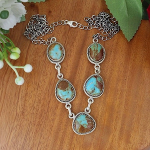 May include: A silver necklace featuring five turquoise and brown oval-shaped stones. The stones are set in a silver rope-style bezel and connected by silver links. The necklace has a silver chain with a clasp.