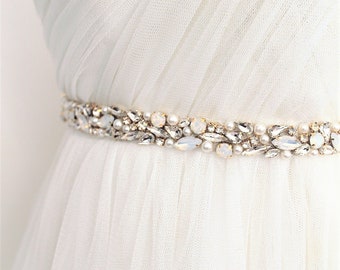 May include: A white tulle wedding dress with a beaded belt featuring clear and iridescent stones.