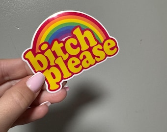 May include: A sticker with a rainbow design and the words "bitch please" in yellow, outlined in red. The sticker has a white border and is held by a hand with pink nail polish.
