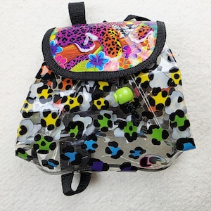 May include: A clear plastic mini backpack featuring a colorful leopard print pattern with black, yellow, blue, and green spots. The top flap displays a leopard resting on a branch surrounded by tropical flowers, secured by a bright green toggle.