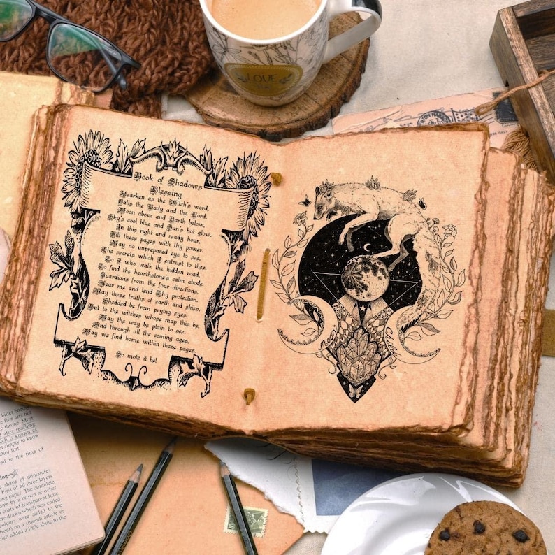 May include: An open, aged-looking book with the title "Book of Shadows" and decorative illustrations. The right page features a wolf and moon design. A cup of coffee, glasses, and pencils are also visible.