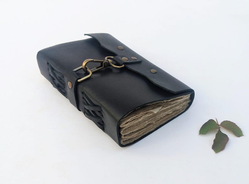 May include: A black leather journal with a clasp closure. The journal has a flap that secures with a metal clasp. The edges of the journal are stitched with a woven design. The pages are aged.