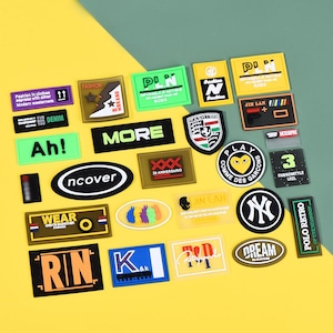 May include: A collection of various colorful fabric patches with text and graphics. Designs include the words "FASHION", "MORE", "WEAR", and "DREAM", along with other logos and symbols. The patches are in various shapes and sizes.