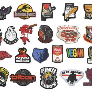 Op de afbeelding: Collectie van diverse patches met diverse ontwerpen. Inclusief een zwarte adelaar, een dinosaurus uit Jurassic Park, een tank, een surfplank, een militair voertuig, een hond, een spook, een honkbalspeler, een cobra, een auto, een beer en meer.