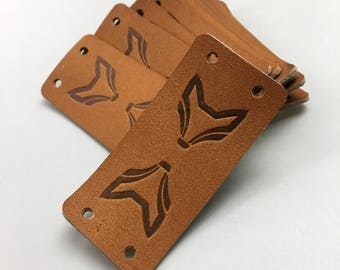 May include: A stack of brown leather labels with a fox design and holes for stitching.