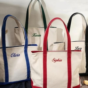 Può includere: Una collezione di borse tote personalizzate in vari colori. Le borse sono bianco sporco con finiture e manici colorati. Ogni borsa ha un nome ricamato in un colore coordinato. I nomi includono Olivia, Keven, Sophia e Lucy.