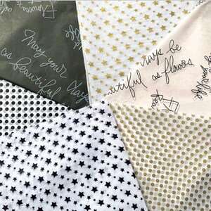 May include: Assortment of tissue paper with different patterns, including gold stars on white, black stars on white, gold polka dots on white, and black polka dots on white. The tissue paper has handwritten messages in black ink, including "May your day be as beautiful as flowers".