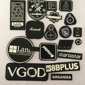 以下が含まれることがあります： 様々なロゴとテキストが施された、白と黒のパッチのコレクションです。「Black Helmet」、「Marshall」、「Lane Furniture」、「Bristol」、「VGOD」、「Subtle」などのパッチが含まれています。幾何学模様のものもあれば、テキストだけのものもあります。