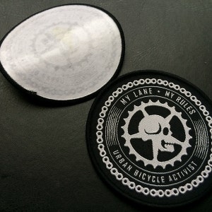 May include: A black and white embroidered patch with a skull and gears. The text reads "My Lane + My Rules Urban Bicycle Activist".