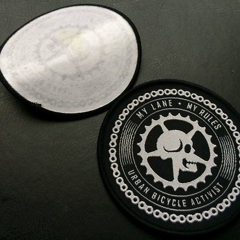 May include: A black and white embroidered patch with a skull and gears. The text reads "My Lane + My Rules Urban Bicycle Activist".