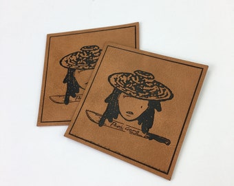 May include: Two brown leather patches with black ink illustrations of a person wearing a hat and holding a knife. The text "Papi Gang" is printed on the bottom of the patch.