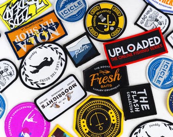 May include: An assortment of colourful embroidered patches with various designs and text, including "The Flash Collective", "Fresh Baits", "Take The Reins", "Uploaded The Online Fishing Series", "Fly Shop NOLA", "Moodricht's", "Palm", "Icicle Brewing Company", and "Naomh Mearnós".