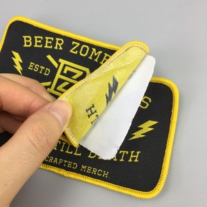 Könnte beinhalten: Schwarzer und gelber gestickter Aufnäher mit dem Text "Beer Zombies Est. Till Death Crafted Merch" und einer Blitzgrafik.