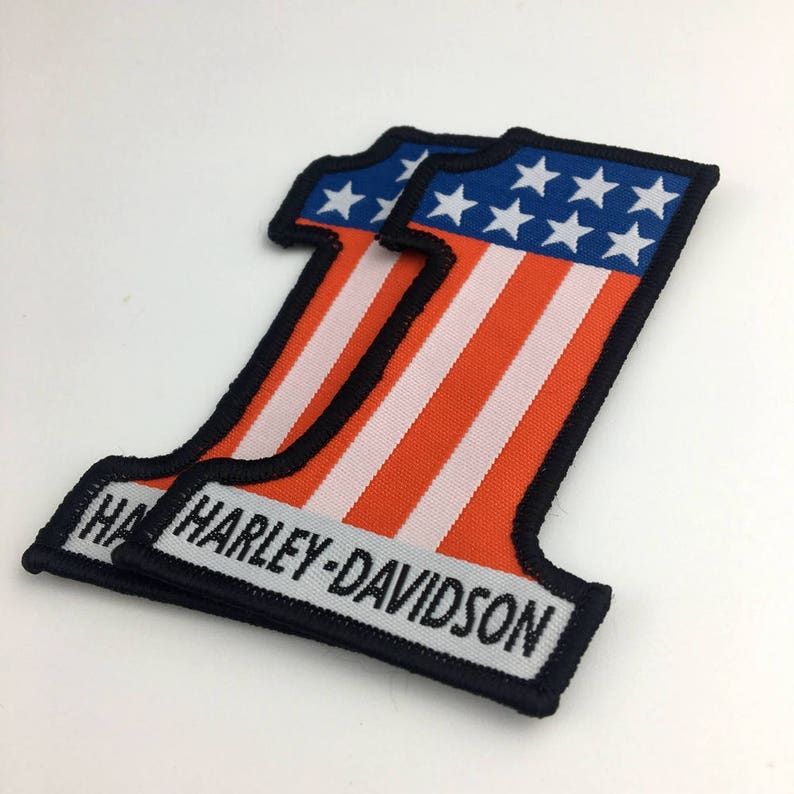 May include: Two black-bordered patches with an American flag design in the shape of the number one. The patches have the text "Harley-Davidson" in white lettering.