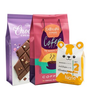 Peut inclure: Trois sacs color&eacute;s de produits alimentaires. Un sac violet de chocolat avec le mot "Chocolate" et un graphique de barre chocolat&eacute;e. Un sac rose de caf&eacute; avec le mot "Coffee" et un graphique de tasse &agrave; caf&eacute;. Un sac blanc et jaune avec un graphique d'ours et le mot "Nate".