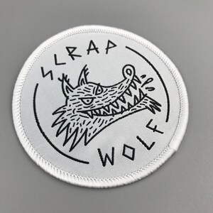 May include: White embroidered patch with a black outline of a snarling wolf with the text "TRAP WOLF" around it.