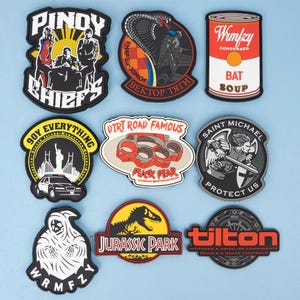 May include: A selection of patches with diverse designs. Features a patch with the text "PINOY CHIEFS", a cobra, a can of "BAT SOUP", a New York City themed patch, a brass knuckles patch with "FUCK FEAR", a Saint Michael patch, a Grim Reaper patch, a "JURASSIC PARK" patch, and a "tilton" patch.