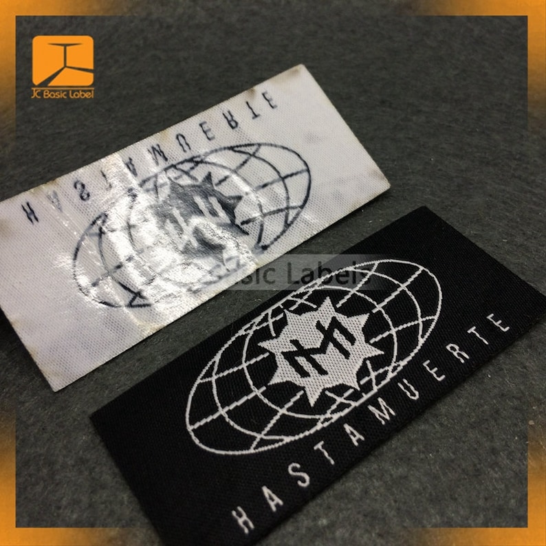 May include: Two woven fabric labels with a white globe design and a star with the letters "RM" inside. The top label is white with black text that reads "HY8JWMOEBIE". The bottom label is black with white text that reads "HASTA MUERTE".