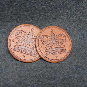 Könnte beinhalten: Zwei braune Lederpatches mit einem Kronendesign und dem Text "King & Queen".