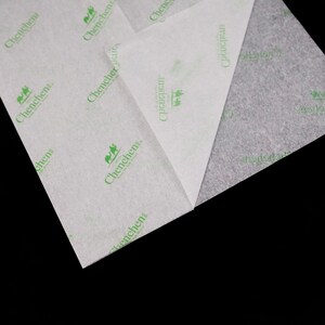 May include: Close-up of two sheets of white tissue paper with a green logo that says "Chenchen, Trust of Quality Life" printed on them. The tissue paper is folded in half and the edges are visible.
